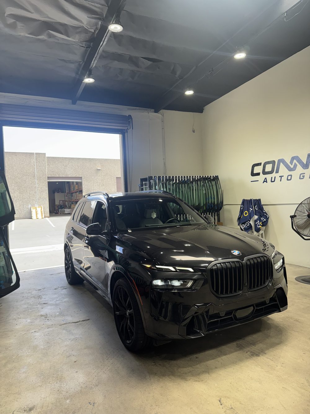 A BMW X7 in the Connect Auto Glass shop with the glass racks behind it